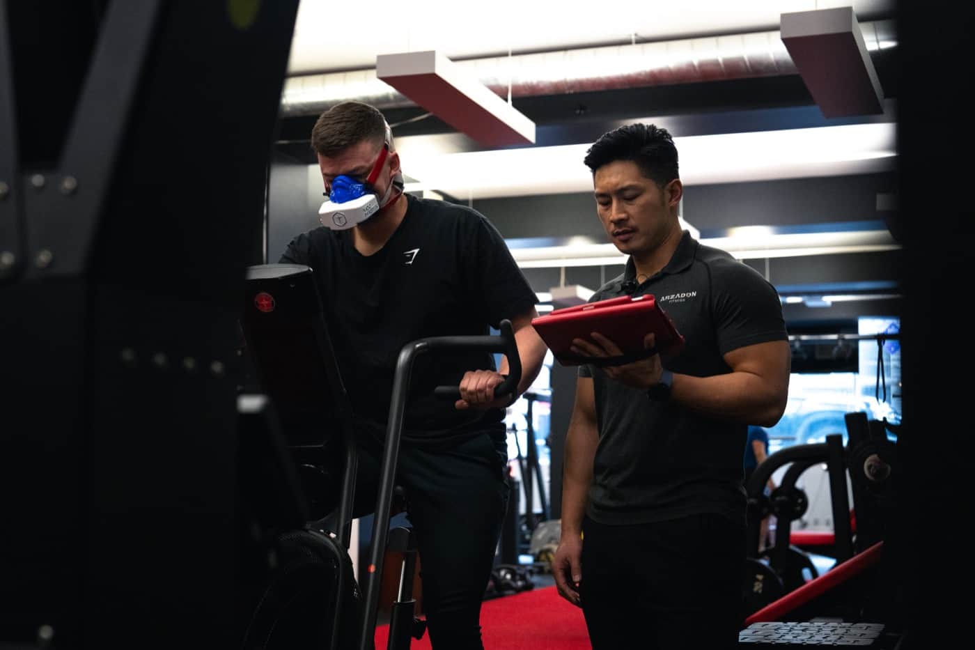 Trainer monitors VO2 max test as masked client pedals air bike