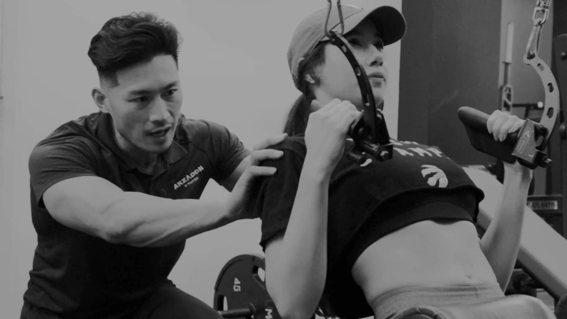 Black-and-white trainer guiding female client's form on incline machine's form during a one-on-one fat loss training session in Toronto