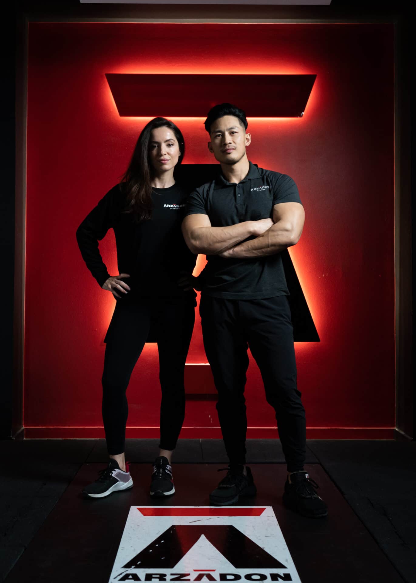 Jennifer Arzadon, Co-Founder of Arzadon Fitness, standing with Jay Arzadon before the illuminated Arzadon A-logo in the Toronto studio