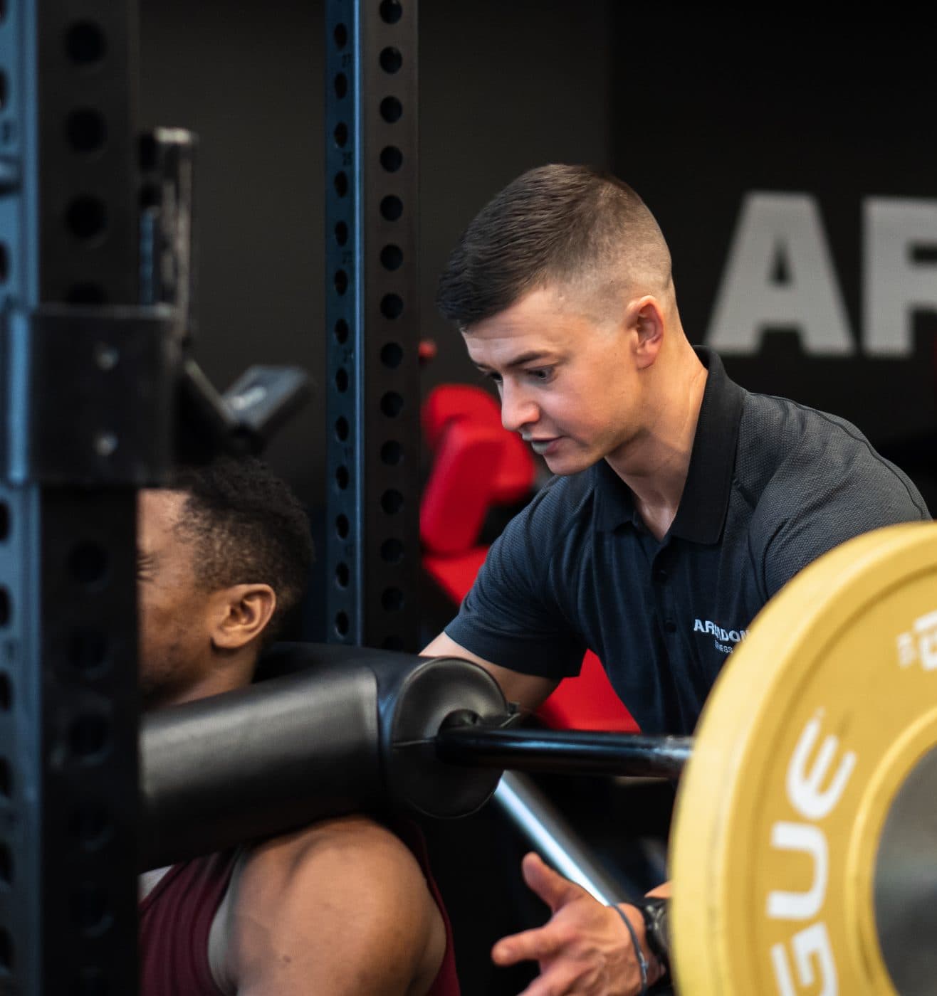 Coach cueing a male client through a barbell squat in the power rack during a hybrid coaching session at Arzadon Fitness Toronto