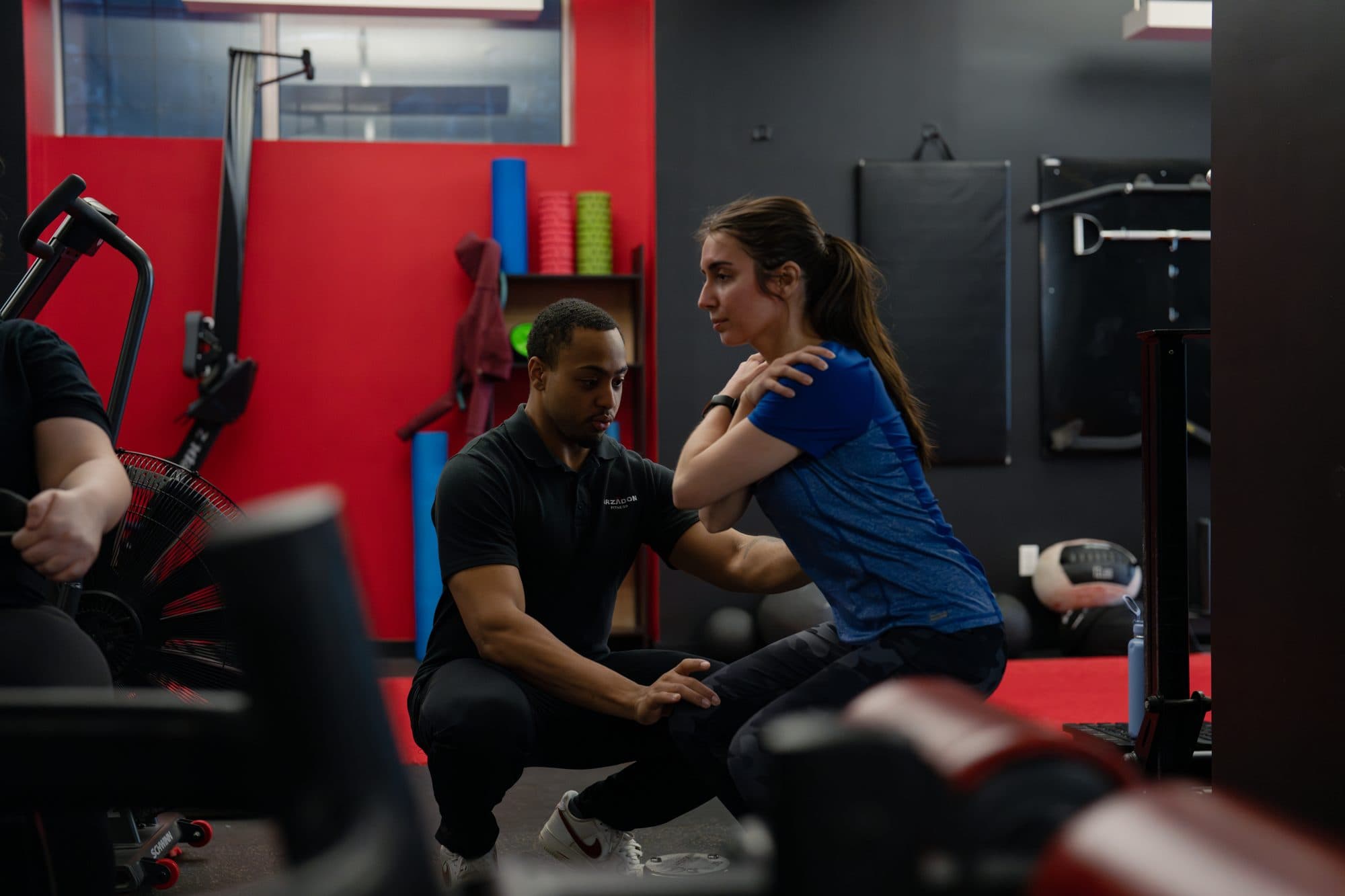Arzadon Fitness coach hands-on correcting a client's squat form during a personal training session in Toronto
